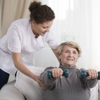 Old woman training with physiotherapist at home